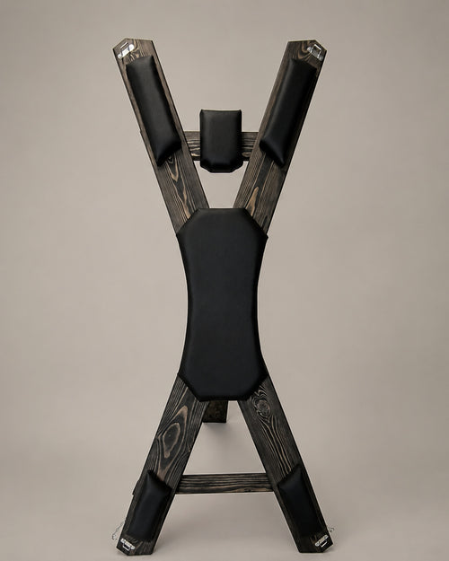Front view of a freestanding St. Andrew’s Cross in dark-finished spruce with black padded supports