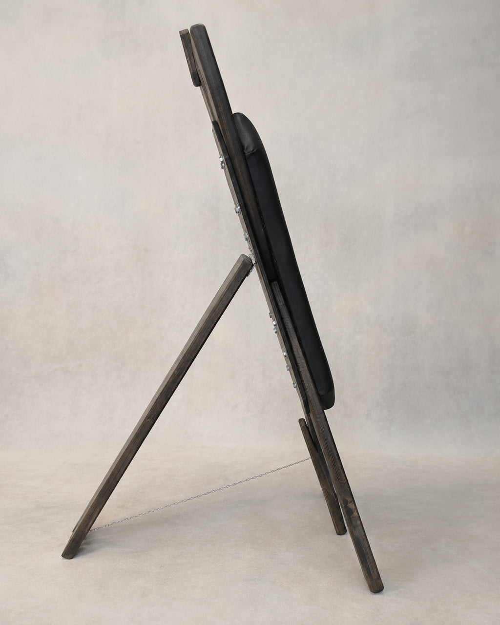 Side view of a freestanding St. Andrew’s Cross showing the rear support, black padded sections and stabilizing chain